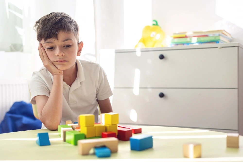 A young boy who is a YBL Behaviour Support participant rests his head on his hand while sitting with building blocks