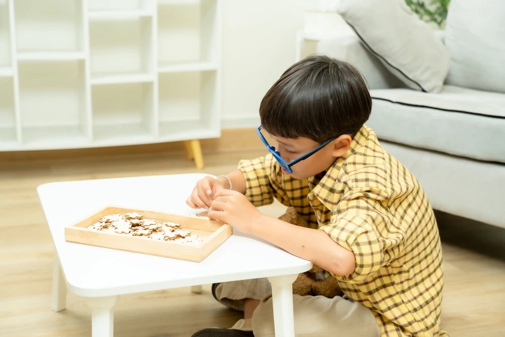 A YBL Behaviour Support participant, a young boy, sits on the floor concentrating on a puzzle