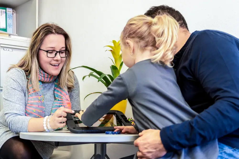 A YBL Behaviour Support team member and a father help a young participant play a game on a tablet