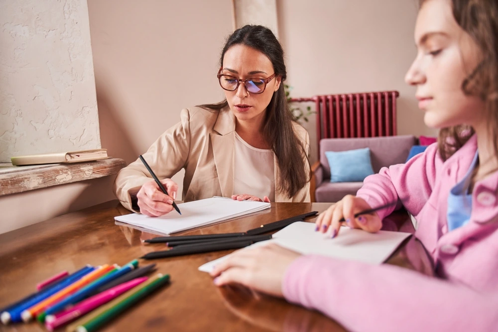 A YBL Behaviour Support team member draws with a young participant at a wooden table with coloured pencils