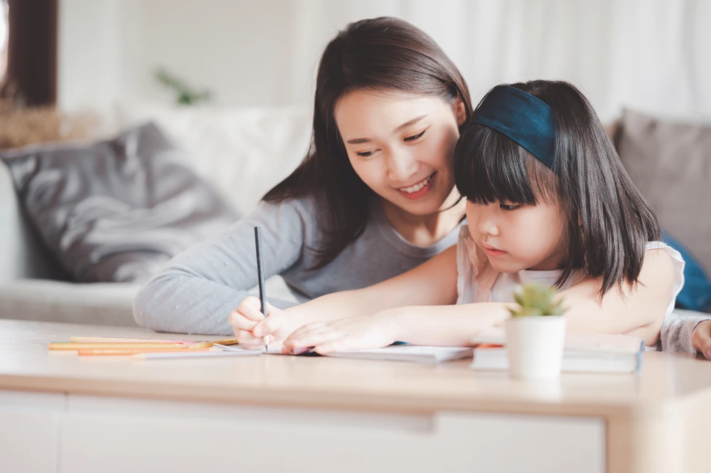 A YBL Behaviour Support team member helps a young participant with her writing or drawing at a table
