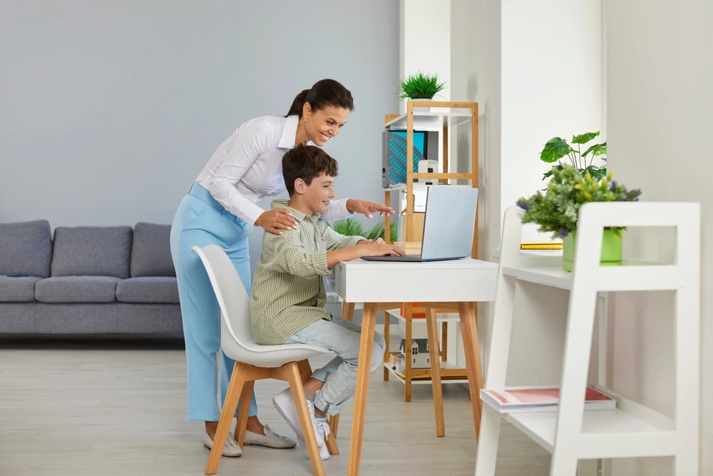 A YBL Behaviour Support team member helps a young male participant with a laptop in a living room or home office