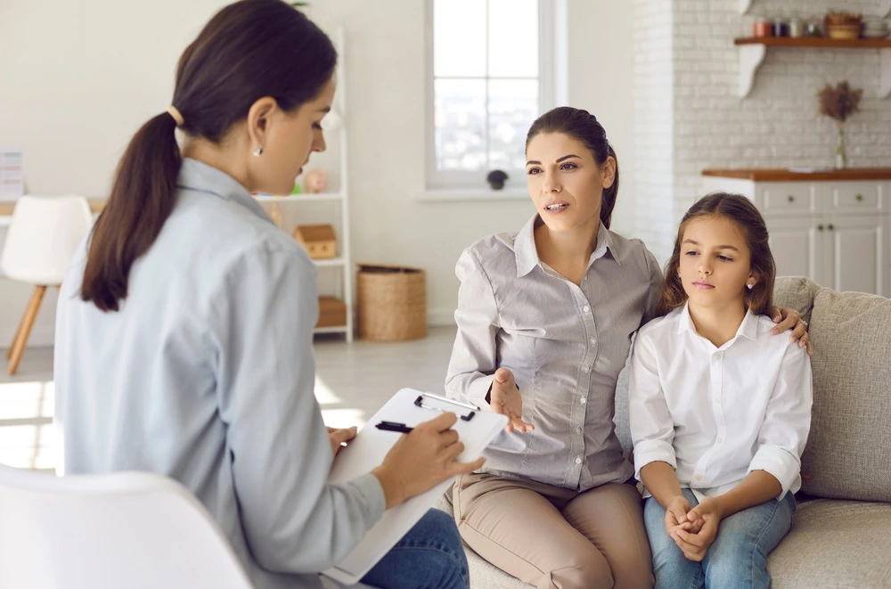 Parent sitting on sofa with preteen child and talking to counseling psychologist of YBL BS